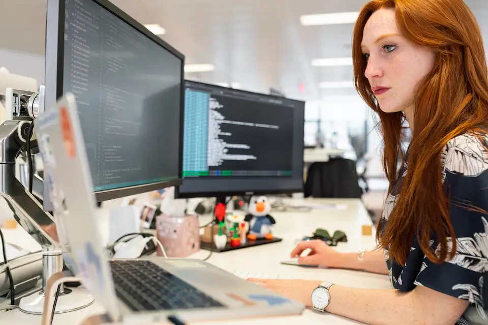 Woman with red hair looking at multple monitors